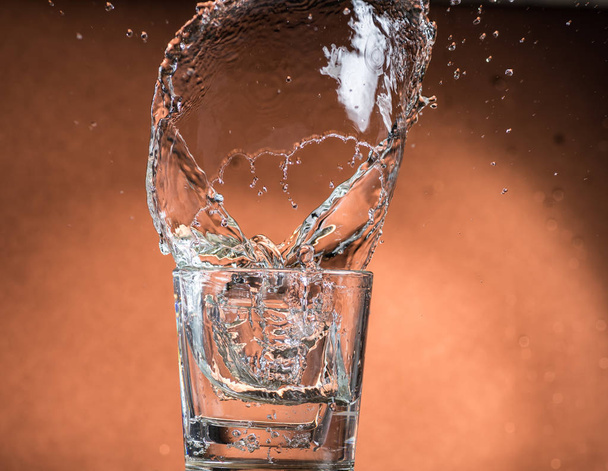 splash in a glass of whiskey with ice on an orange brown background - 写真・画像
