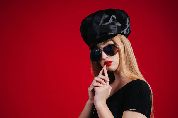 Sexy strict woman with red lips with black hat on red background - Фото, зображення
