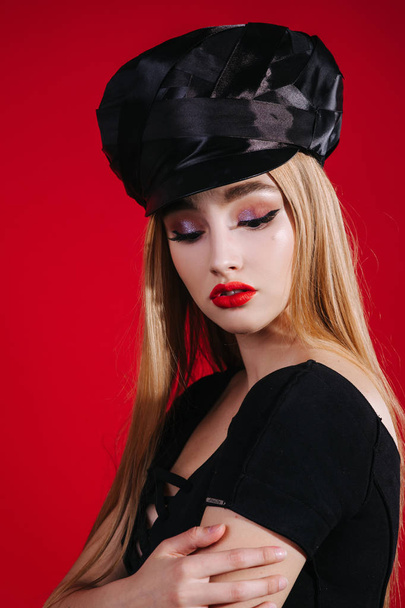 Sexy strict woman with red lips with black hat on red background - Фото, изображение