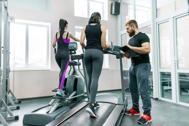 Young smiling fitness women with personal trainer an adult athletic man on treadmill in the gym. Sport, teamwork, training, healthy lifestyle concept - Foto, immagini