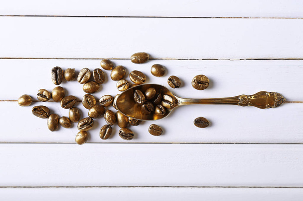 Spoon and golden coffee beans on white wooden background - Photo, Image
