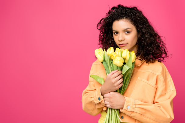attractive curly african american girl holding yellow tulips isolated on crimson - Photo, Image