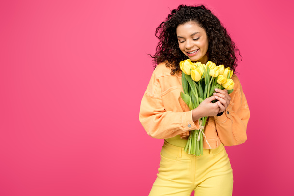 smiling african american girl holding yellow tulips isolated on crimson - Foto, immagini