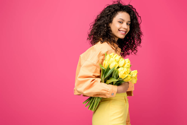 smiling african american woman holding yellow tulips isolated on crimson - Foto, imagen