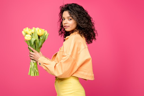 attractive african american woman holding yellow tulips isolated on crimson - Photo, Image