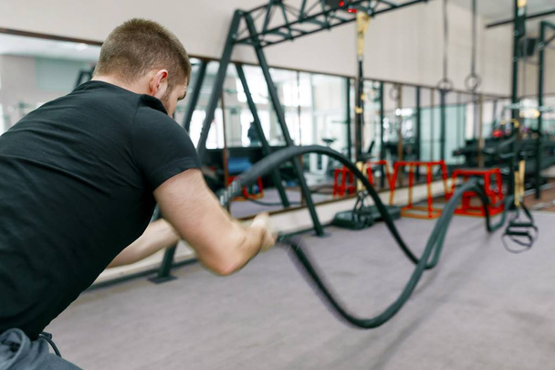 Athletic muscular bearded man exercising in the gym with battle ropes. Sport, training, people, healthy lifestyle concept. - Φωτογραφία, εικόνα