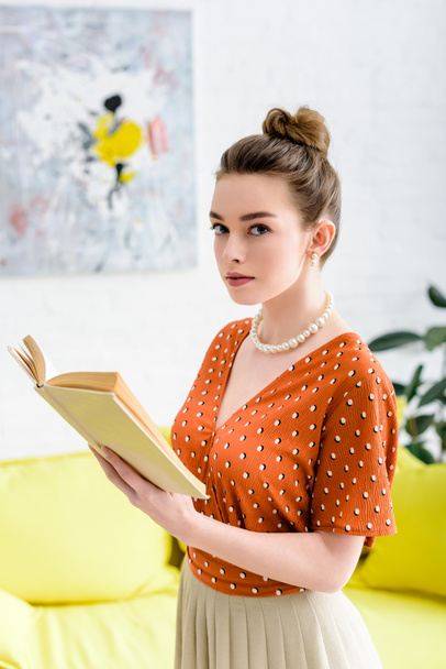 atraktivní elegantní mladá žena drží knihu a při pohledu na fotoaparát - Fotografie, Obrázek