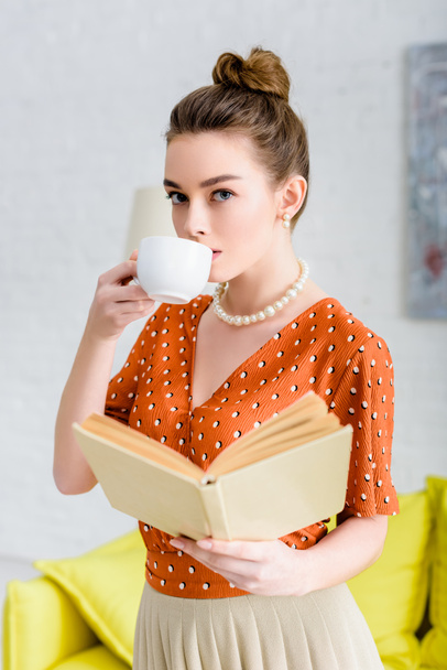 elegante jongedame in parelketting holding boek en koffie drinken - Foto, afbeelding
