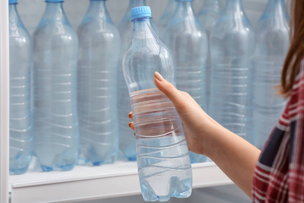 Woman taking bottle of water from fridge in shop - Foto, afbeelding