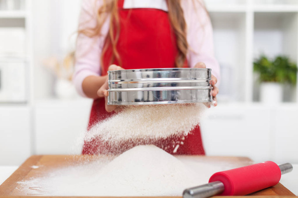 Girl sifting flour in the kitchen using a metallic sieve - Zdjęcie, obraz