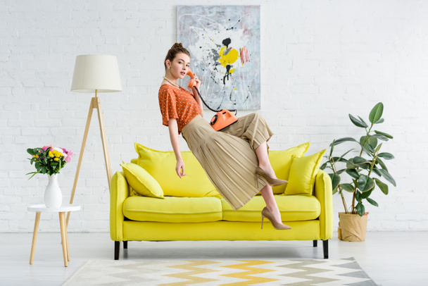 elegant young woman levitating in air and talking on vintage phone in living room - Foto, Bild