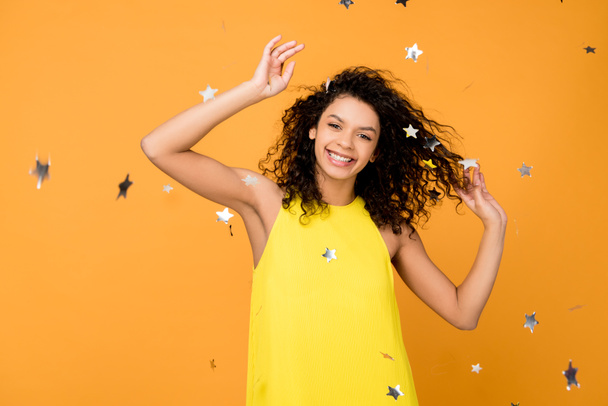 happy curly african american woman smiling near shiny confetti stars on orange  - Photo, Image