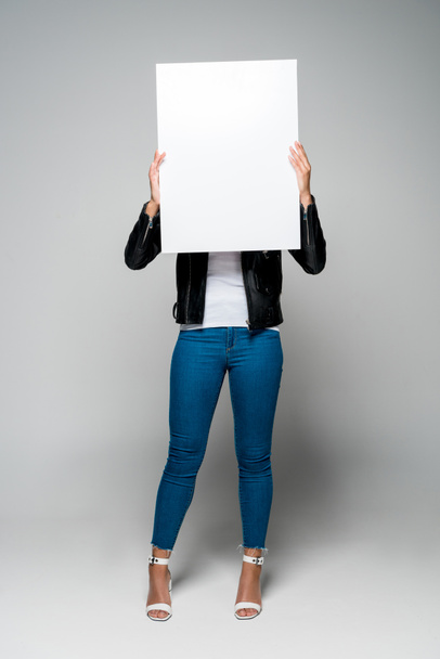 african american young woman covering face with blank placard while standing on grey - Zdjęcie, obraz