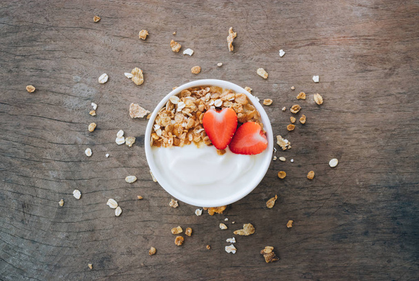 Vista superior del yogur en un tazón de madera con granola, fresa fresca sobre una mesa de madera blanca. Concepto de alimentos saludables
. - Foto, Imagen