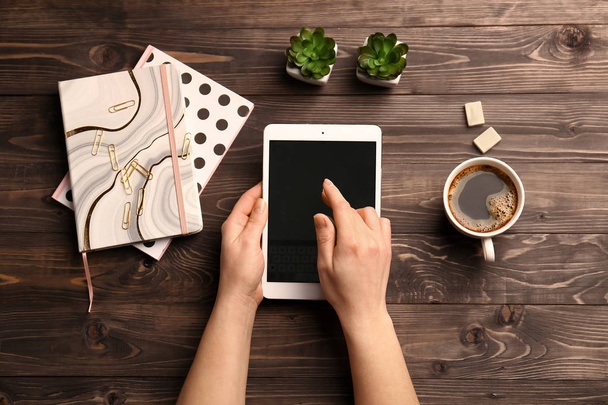 Mãos femininas com computador tablet, xícara de café e cadernos em fundo de madeira
 - Foto, Imagem