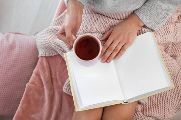 Jovem mulher bebendo chá quente enquanto lê livro em casa
 - Foto, Imagem