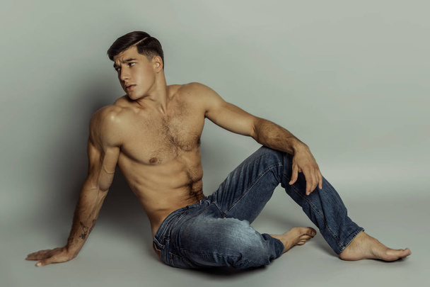 Muscle strong beautiful stripped male model in denim blue jeans with black t-shirt on grey isolated font background - Φωτογραφία, εικόνα