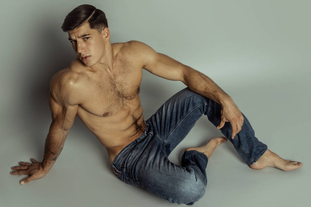 Muscle strong beautiful stripped male model in denim blue jeans with black t-shirt on grey isolated font background - Photo, Image