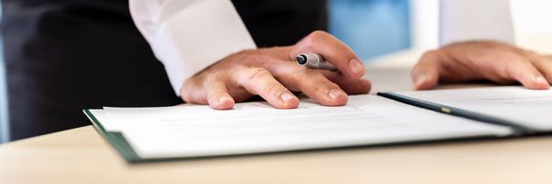 Imagem ampla do empresário segurando caneta de tinta apoiada em um docu
 - Foto, Imagem