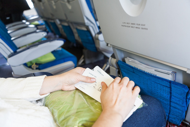 Caucasian female sitting in aircraft with boarding passes in hands - Foto, Bild