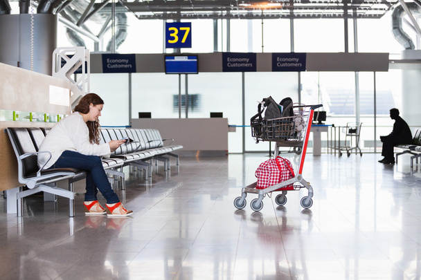 Woman waiting flight in airport lounge with luggage hand-cart - Foto, Bild