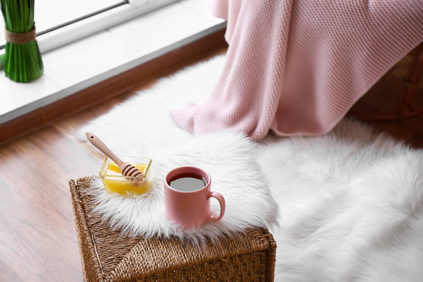 Cup of hot tea and honey on wicker box in room - Photo, Image