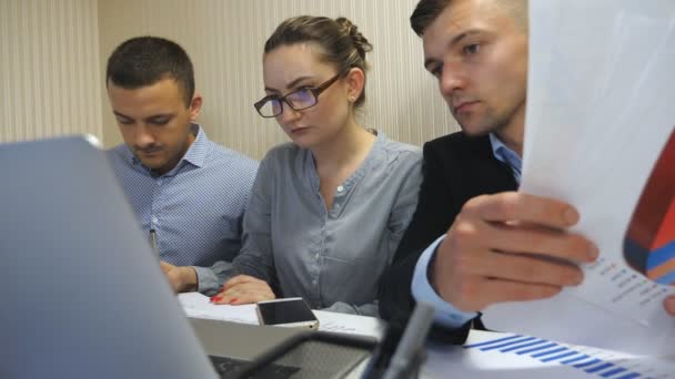 Group of young business people sitting at table in modern office and working on new project. Colleagues carefully review the documentswhile working process. Office workers busy developing business - Footage, Video