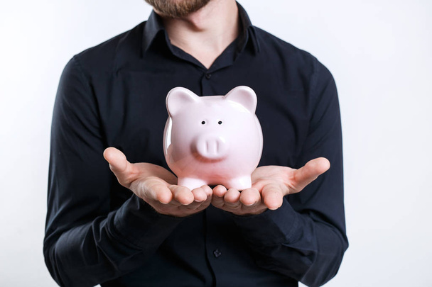 Businessman in black shirt holding a piggy bank. Saving money - Фото, изображение