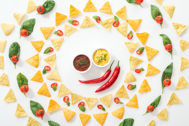top view of tasty nachos, sauces and sliced chili peppers with basil and cherry tomatoes  - 写真・画像