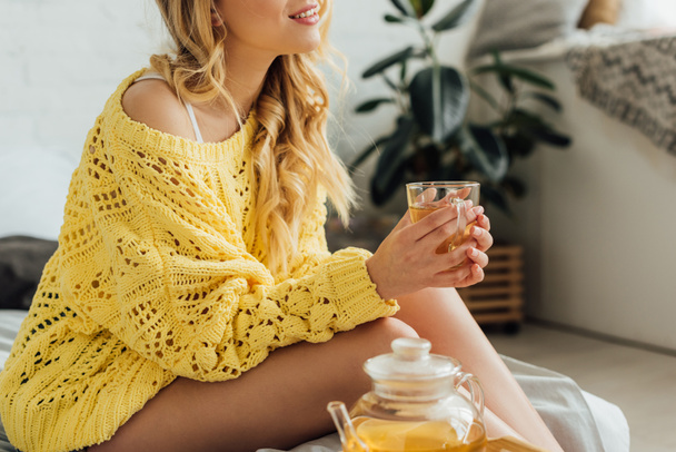 nyírt kilátás a fiatal nő kötött pulóvert ül az ágyban és a gazdaság csésze teát  - Fotó, kép