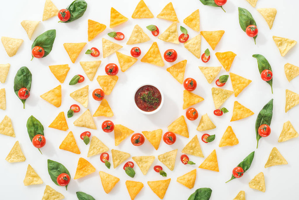 flat lay with tasty nachos, sauce and sliced chili peppers with basil and cherry tomatoes on white background  - Fotografie, Obrázek