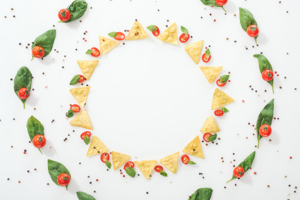 acostado plano con sabrosos nachos, especias y chiles en rodajas con hojas de albahaca y tomates cherry maduros
 - Foto, Imagen