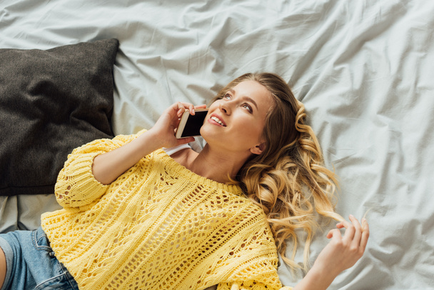 beautiful smiling girl lying in bed and talking on smartphone - Fotoğraf, Görsel
