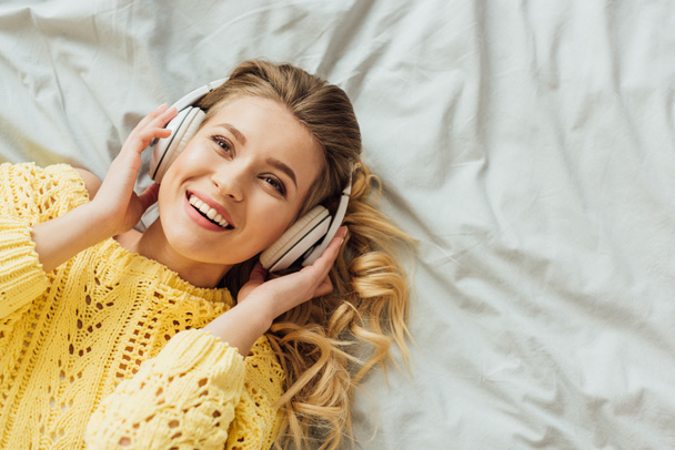 top view of beautiful smiling young woman in headphones lying in bed and listening music with copy space - Фото, изображение