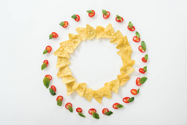 pohled na plátky chilli papriček a chutných nachos s bazalkovým listím na bílém pozadí  - Fotografie, Obrázek
