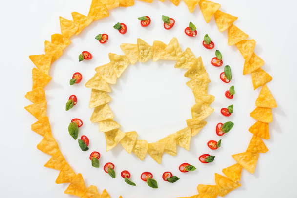 top view of sliced chili peppers and tasty nachos with basil leaves on white background  - Foto, Bild
