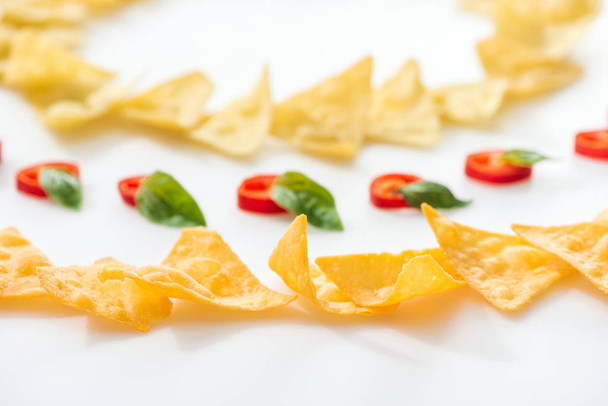 selective focus of tasty nachos and chili peppers with basil on white background  - Foto, Bild