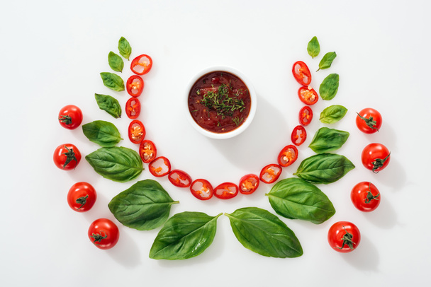 flat lay with cut chili peppers, basil leaves, sauce and ripe cherry tomatoes on white background  - Foto, Bild