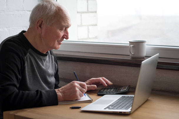 Un anciano que cuenta con una calculadora e introduce información en una computadora
. - Foto, Imagen