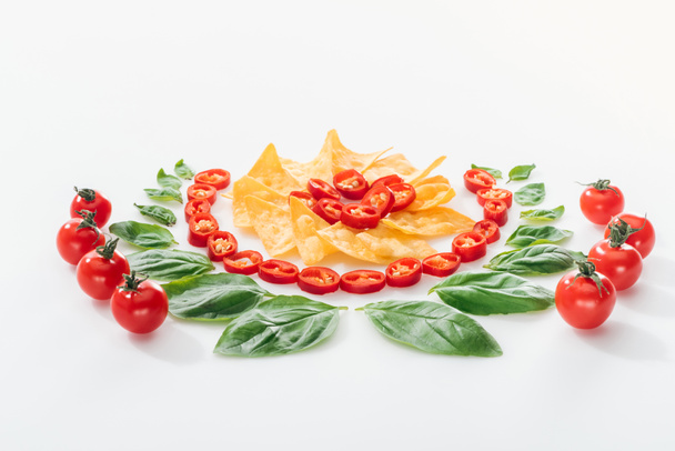 leigos planos com nachos, pimentas cortadas, folhas de manjericão e tomates cereja maduros sobre fundo branco
  - Foto, Imagem