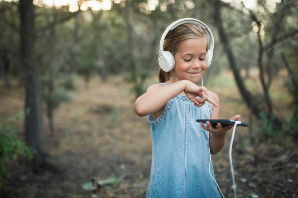 Little girl listening music with her headphones in the forest - Photo, Image