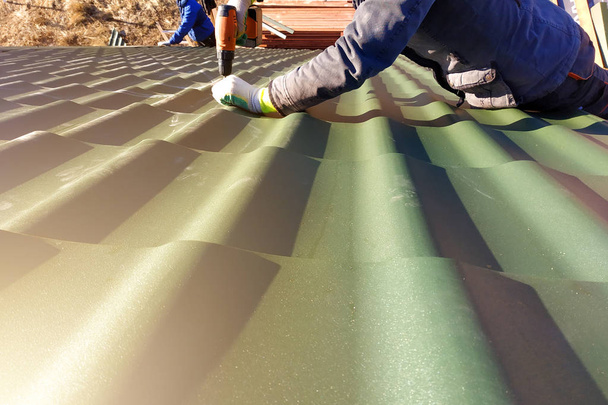 De professionele werknemer werkt aan de installatie van een dak van een dak door bladen van een metal tile en een schroef boren met een boor - Foto, afbeelding