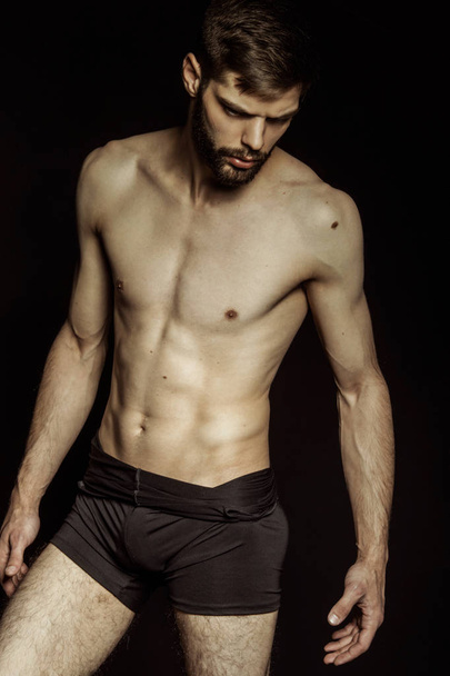 Muscle strong bearded face beautiful stripped male model in black underwear on black isolated font background - Φωτογραφία, εικόνα