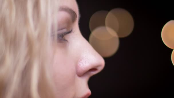Closeup bokorys portrét dospělých atraktivní blondýna kavkazské ženské obrací na kameru s pozadím bokeh při pohledu přímo na kameru - Záběry, video