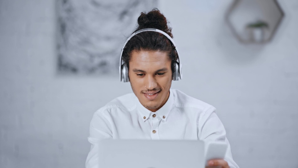 empresário bonito em fones de ouvido ouvir música, usando laptop e smartphone
  - Filmagem, Vídeo