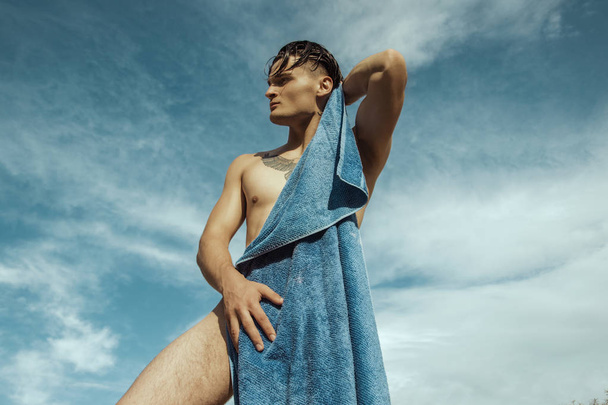 Cara fuerte modelo masculino en el fondo de la naturaleza con arena y agua y cielo en la playa al atardecer
 - Foto, Imagen