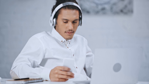 hombre de negocios guapo en auriculares bailando y escuchando música, utilizando el ordenador portátil y el teléfono inteligente
  - Imágenes, Vídeo