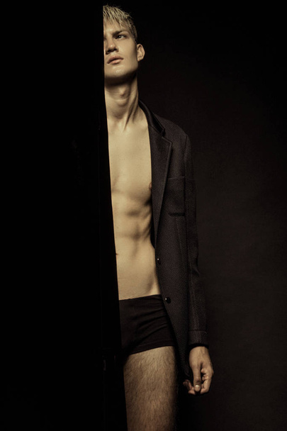 Handsome stripped blonde male model wearing black suit on black isolated font background - 写真・画像