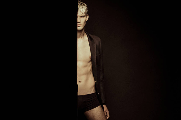 Handsome stripped blonde male model wearing black suit on black isolated font background - Foto, afbeelding