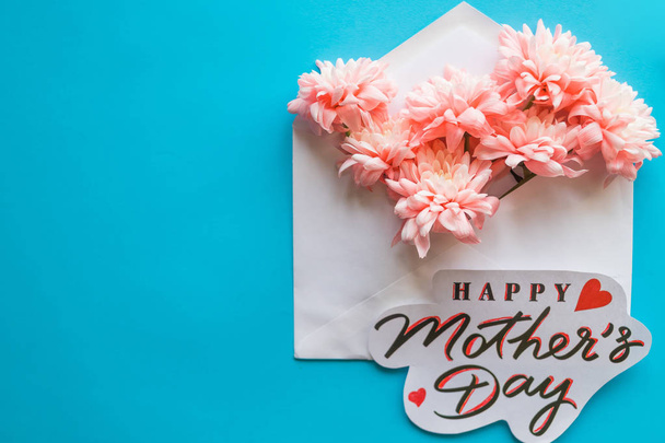 Flores rosadas y tarjeta de felicitación sobre fondo azul. Happy Mothers Day.floral concepto de tarjeta de felicitación, la puesta plana. Día de las madres. tierna imagen primavera
 - Foto, imagen